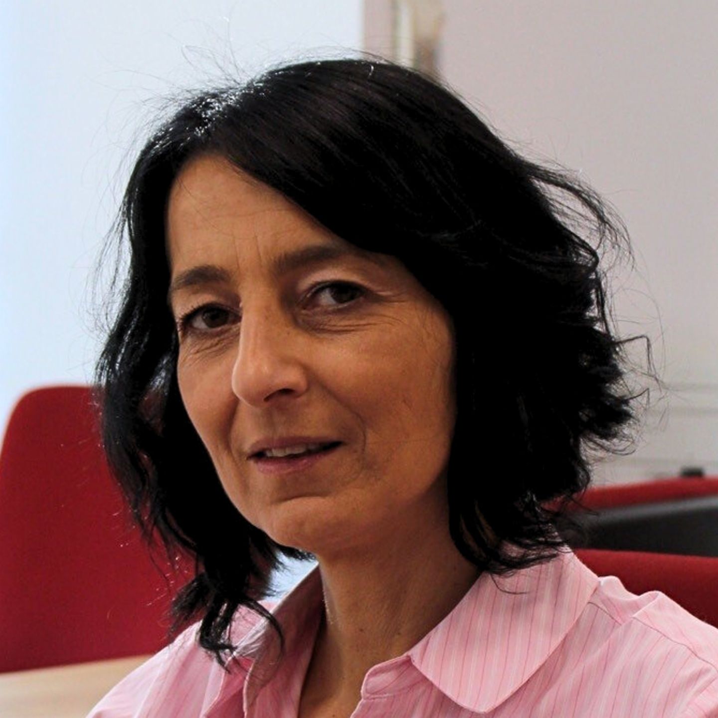Cristina Pasere, Manager of Compliance Operations Support hos EOS Romania, sidder ved sit skrivebord i en pink stribet bluse og kigger på kameraet.