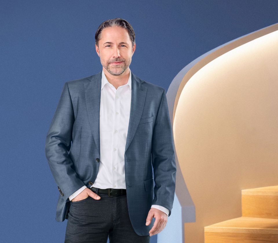 Marwin Ramcke, administrerende direktør for EOS Group, står foran en blå baggrund, klædt i en mørk jakke. Han ser direkte ind i kameraet.