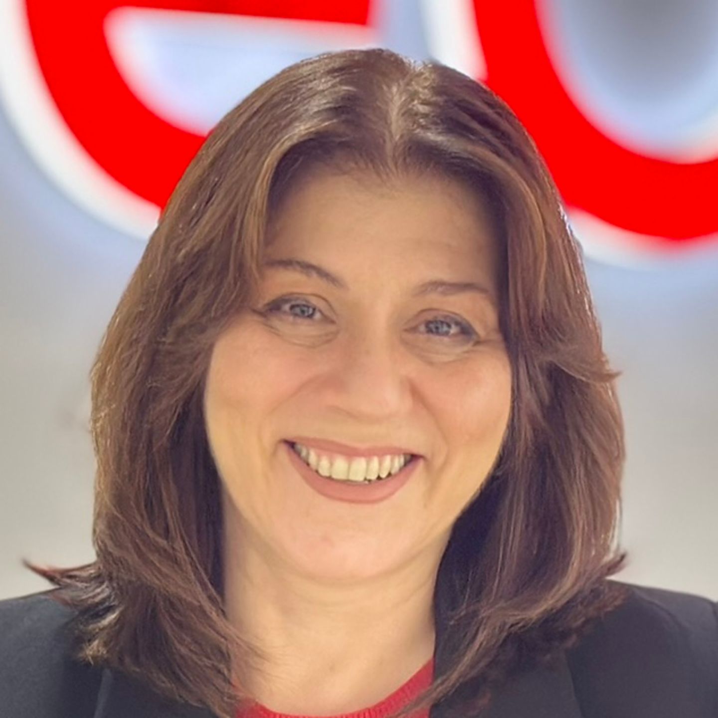 Belén Barreiro, kontaktcenteragent hos EOS i Spanien, læner sig op ad en disk i en sort blazer foran et lyst EOS-logo.