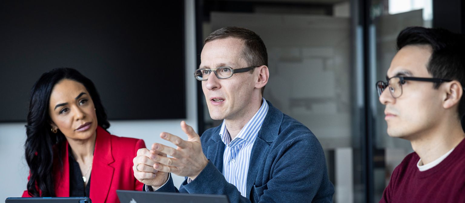 Tre personer fører en samtale på et kontor.