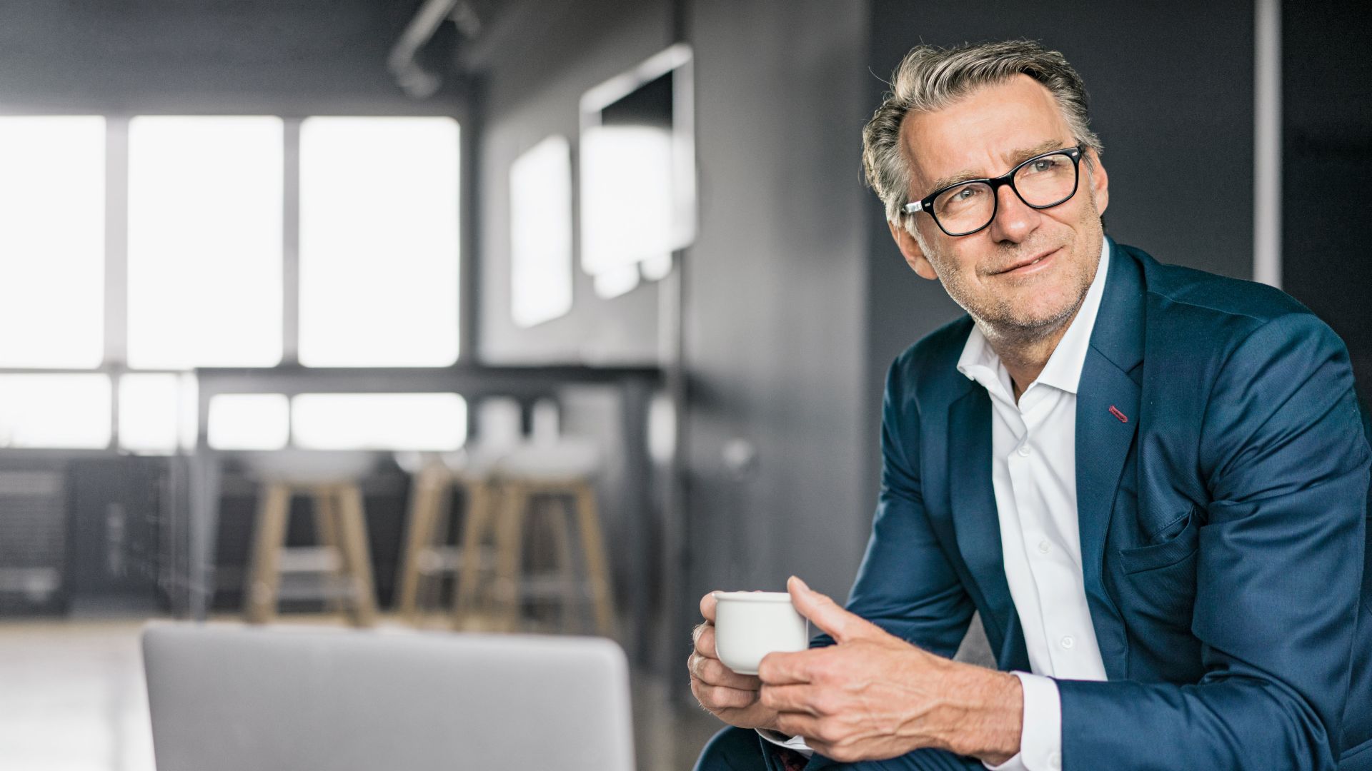 Portrait of a sitting mature businessman wearing a blue suit holding a white coffe cup