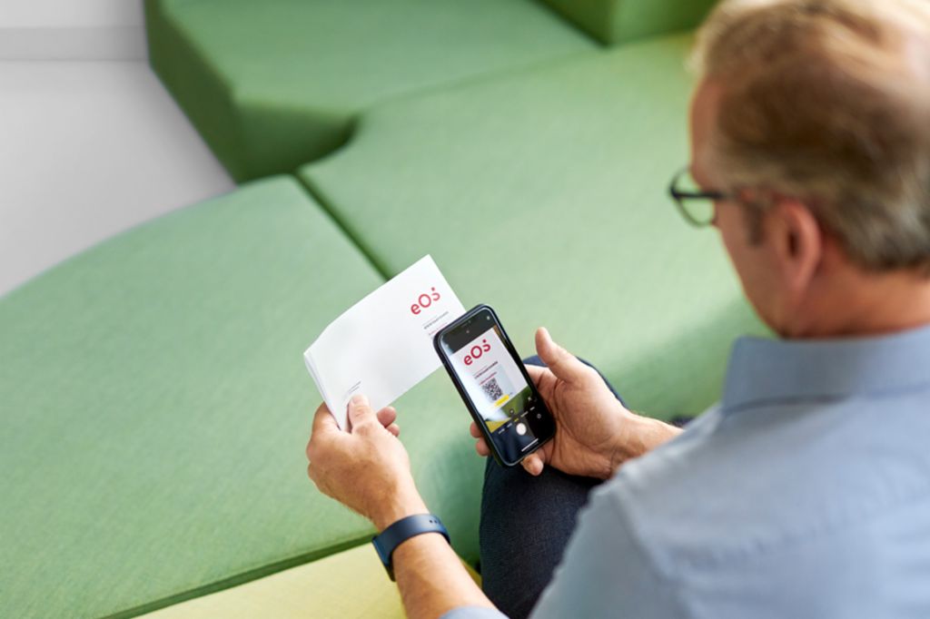 En mand scanner en QR-kode på et brev fra EOS med sin smartphone for at betale sin åbne fordring online på EOS Portalen.