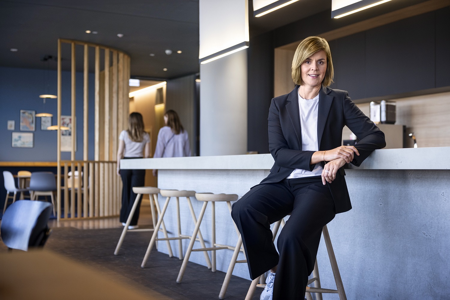 Dr. Eva Griewel, CFO for EOS Gruppen, sidder i et socialt rum på en høj skammel, iført en sort blazer.