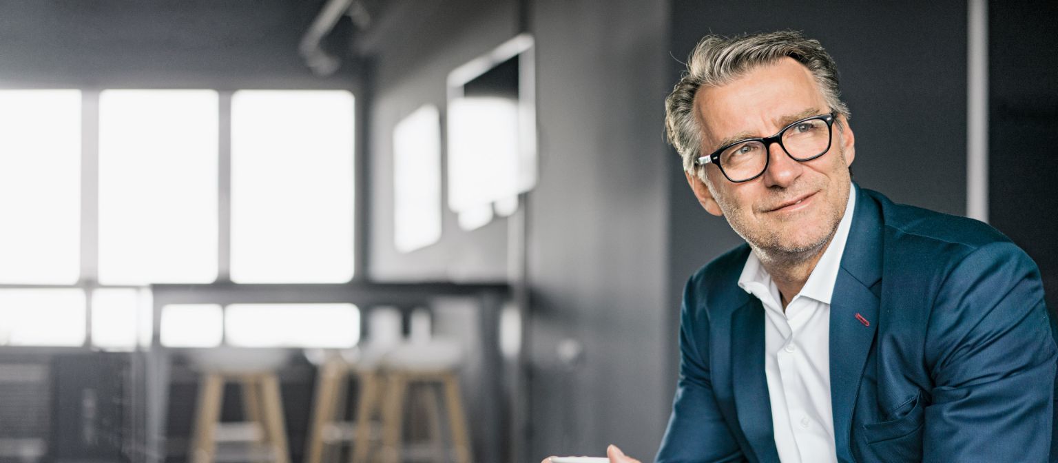 Portrait of a sitting mature businessman wearing a blue suit holding a white coffe cup