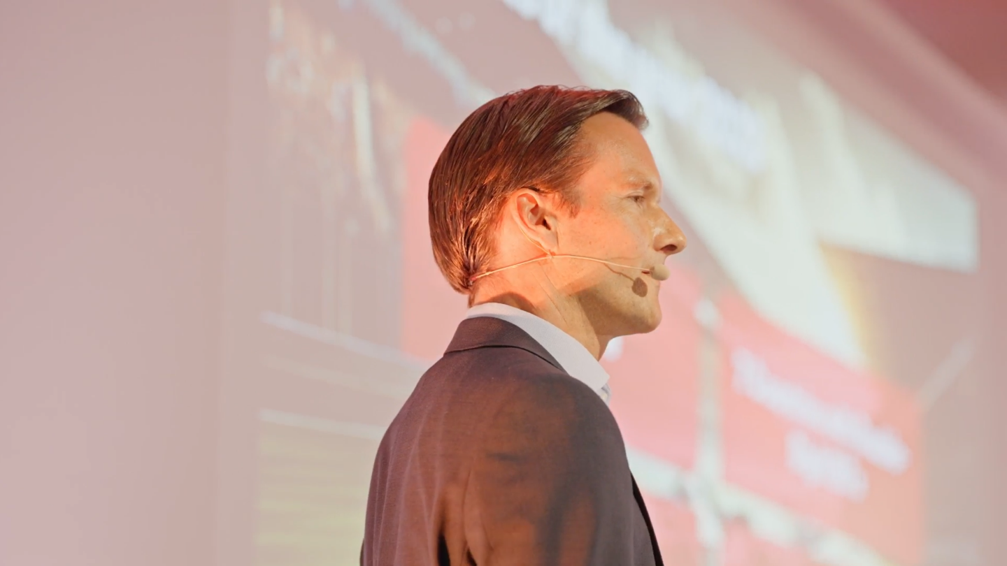 Profile shot of Carsten Tidow, Member of the EOS Group’s Board of Directors and responsible for Eastern Europe, on stage with a microphone and looking to the right. 